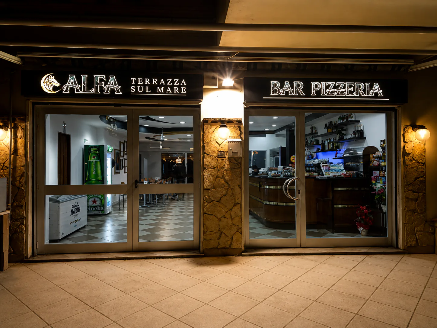L'ingresso di Alfa di sera, con l'insegna illuminata